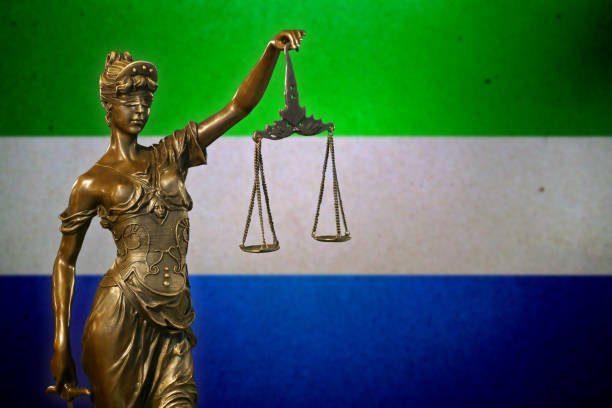 Close-up of a small bronze statuette of Lady Justice before a flag of Sierra Leone.