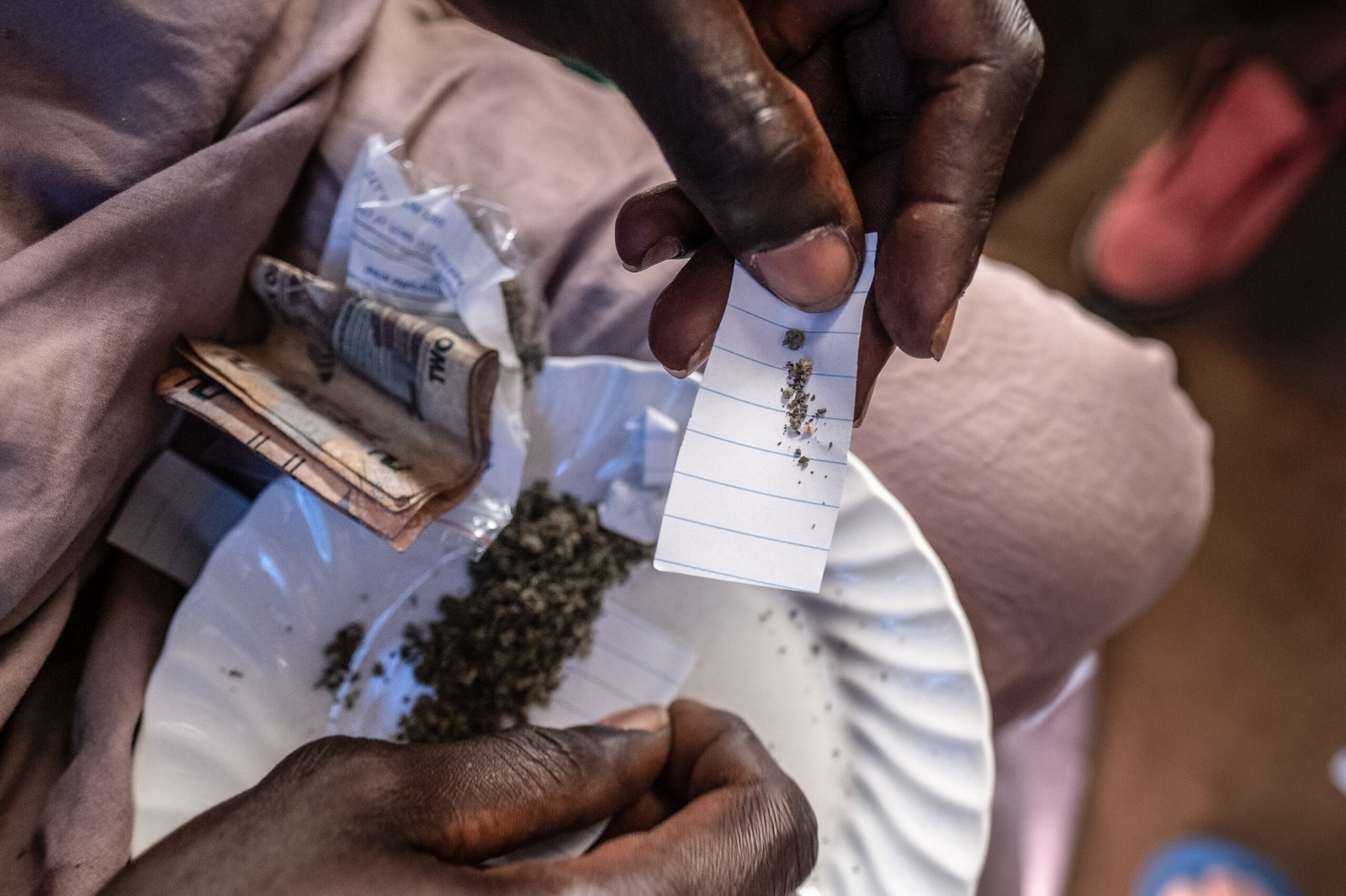 A kush dealer measures out a portion of kush, which will be wrapped in a paper packet and sold for as little as 5,000 Leones (roughly $0.25), in a slum neighbourhood in Freetown, Sierra Leone, on the 24th of September 2023.